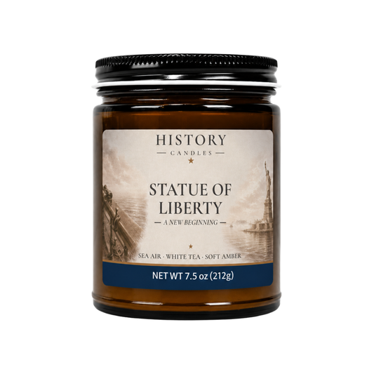 Statue of Liberty History Candle in an amber glass jar with black lid, featuring original harbor artwork and Sea Air, White Tea & Soft Amber fragrance.