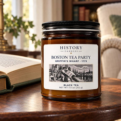 Boston Tea Party candle on a wooden table beside an open book and reading chair in warm window light.